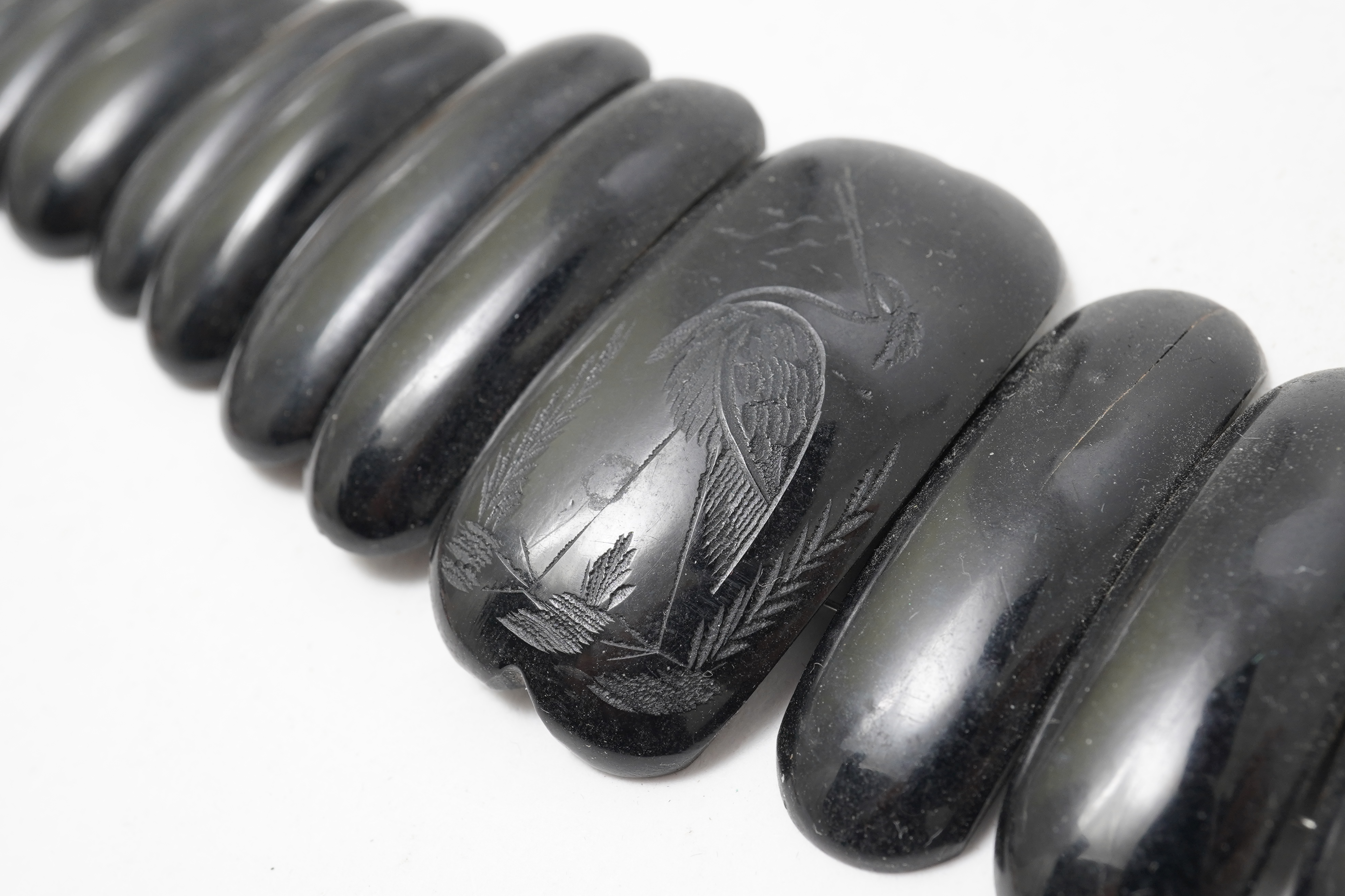 A collection of jewels, comprising: a moulded bog oak brooch depicting a hand holding a posy, length 7.4cm; a carved jet brooch depicting a Gothic ruin, possibly part of Whitby Abbey; a necklace composed of polished pane